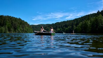 Zwei Personen in einem Ruderboot auf einem idyllischen See im Bayerischen Wald umgeben von Wäldern